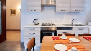 A modern kitchen with white cabinetry, a gas stove, a sink, and a dining area with a wooden table set for two.