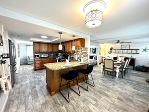A modern kitchen with a central island, bar stools, wooden cabinets, and a hanging light fixture. - Modern & Casual 2BR Near Dearborn St & Beaches (Englewood)
