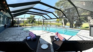 Een buitenzwembadgedeelte met een overdekt terras, twee lounge fauteuils en een tafel met glazen en een bord.