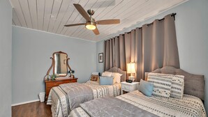 Una camera da letto con due letti, un ventilatore a soffitto, una cassettiera e un comodino con una lampada.