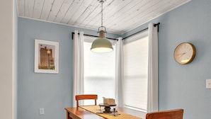 Un'area pranzo con un tavolo e panche in legno, una lampada a sospensione, un quadro appeso al muro e una finestra con tende.