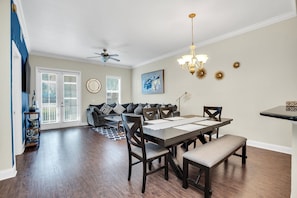 A dining area with a dark wooden table, chairs, and a bench. There is a ceiling fan and a chandelier.