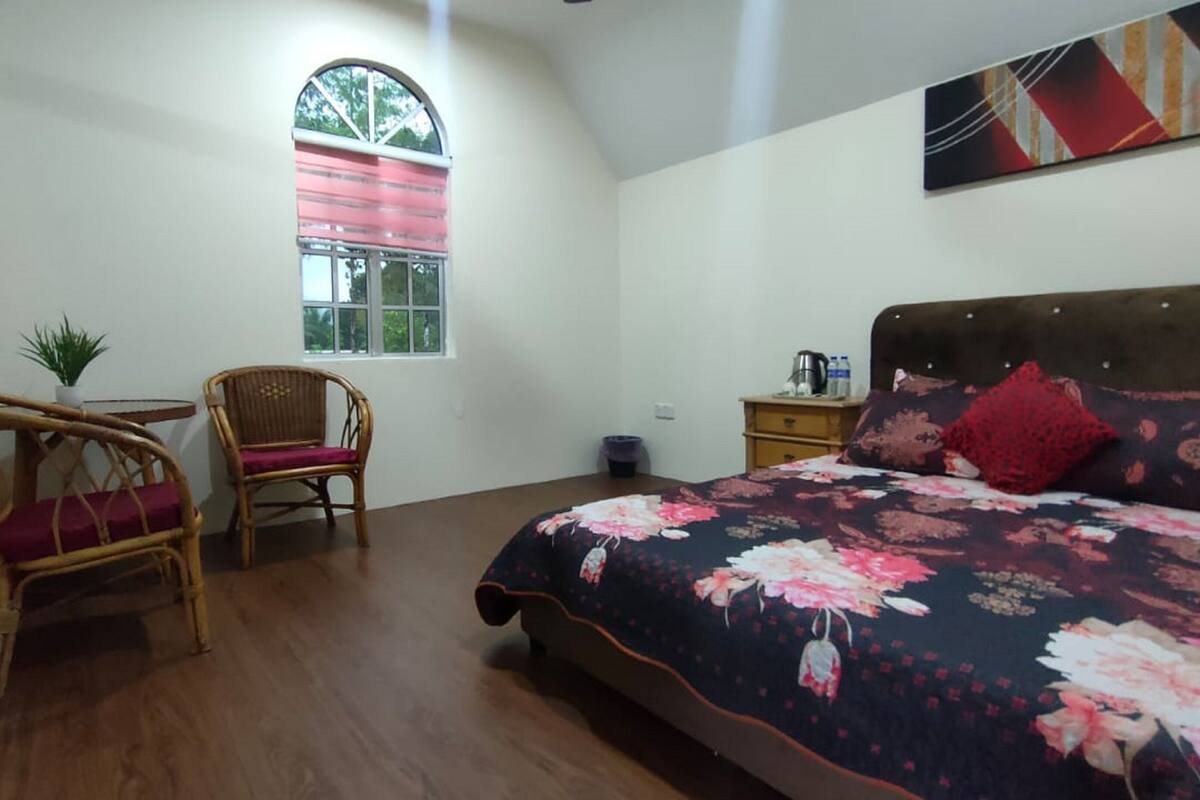 A bedroom with a bed, a chair, a small table, a window, and a wall-mounted artwork.