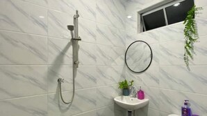 Een badkamer met witte marmeren tegels, een douche, een wastafel, een toilet en een raam met een plant.