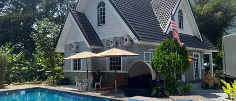 A two-story house with a swimming pool, outdoor furniture, and an American flag.
