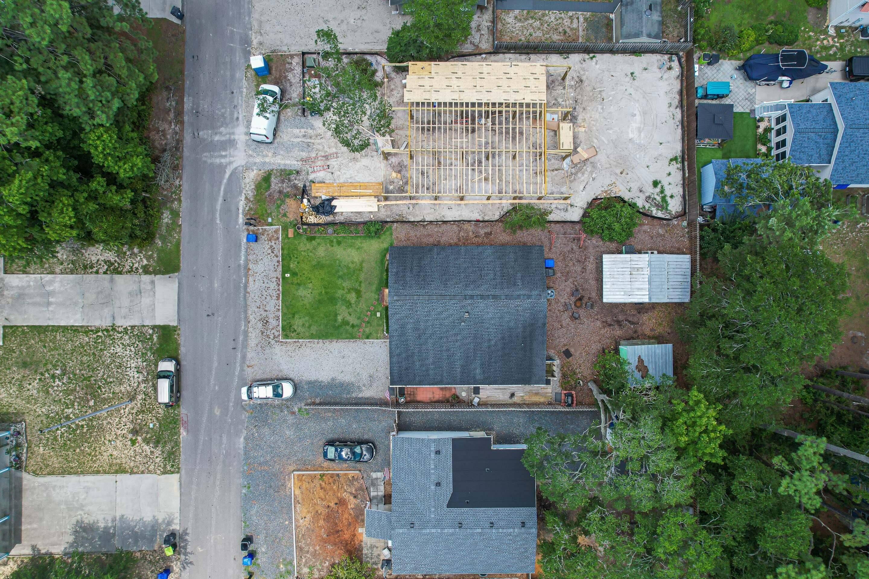 Vista aérea de una zona residencial con una gran área de construcción a cielo abierto, una calle pavimentada y varios coches estacionados.