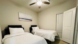 A bedroom with two beds, a ceiling fan, a door, and a wall-mounted artwork.