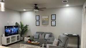 A modern living room with a grey sofa, a coffee table, a TV, and framed artwork on the wall.