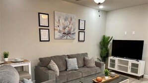A modern living room with a grey sofa, a coffee table, and a flat-screen TV on a white cabinet.