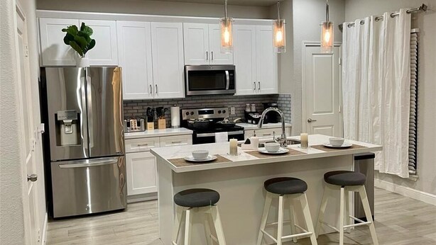 A modern kitchen with white cabinets, stainless steel appliances, and a central island with stools.