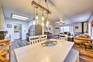 A spacious living area with a large wooden dining table, a sofa, and a kitchen in the background.