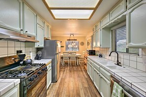A kitchen with white cabinets, a stove, a refrigerator, a dining table with chairs, and a window with blinds.