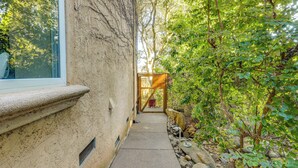 A narrow concrete pathway flanked by a textured wall and dense foliage, leading to a wooden gate. - Santa Rosa Home w/ Private Pool & Tennis Court (Santa Rosa)