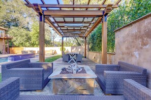 Eine Terrasss mit Feuerstelle, Korbmöbeln und einer Pergola.