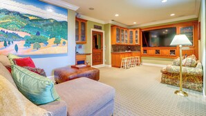 A living room with a large painting, a sofa, a coffee table, and a TV in a kitchen area with wooden cabinets and a bar stool. - Santa Rosa Home w/ Private Pool & Tennis Court (Santa Rosa)