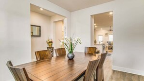 Un comedor con una mesa y sillas de madera, un florero con flores y una cocina al fondo.