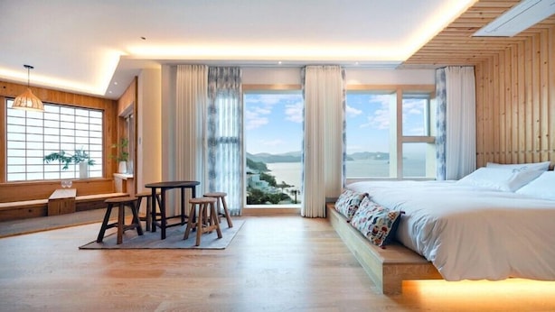 Ein modernes Hotelzimmer mit einem großen Bett, einer Essecke mit Hocker und Meerblick.