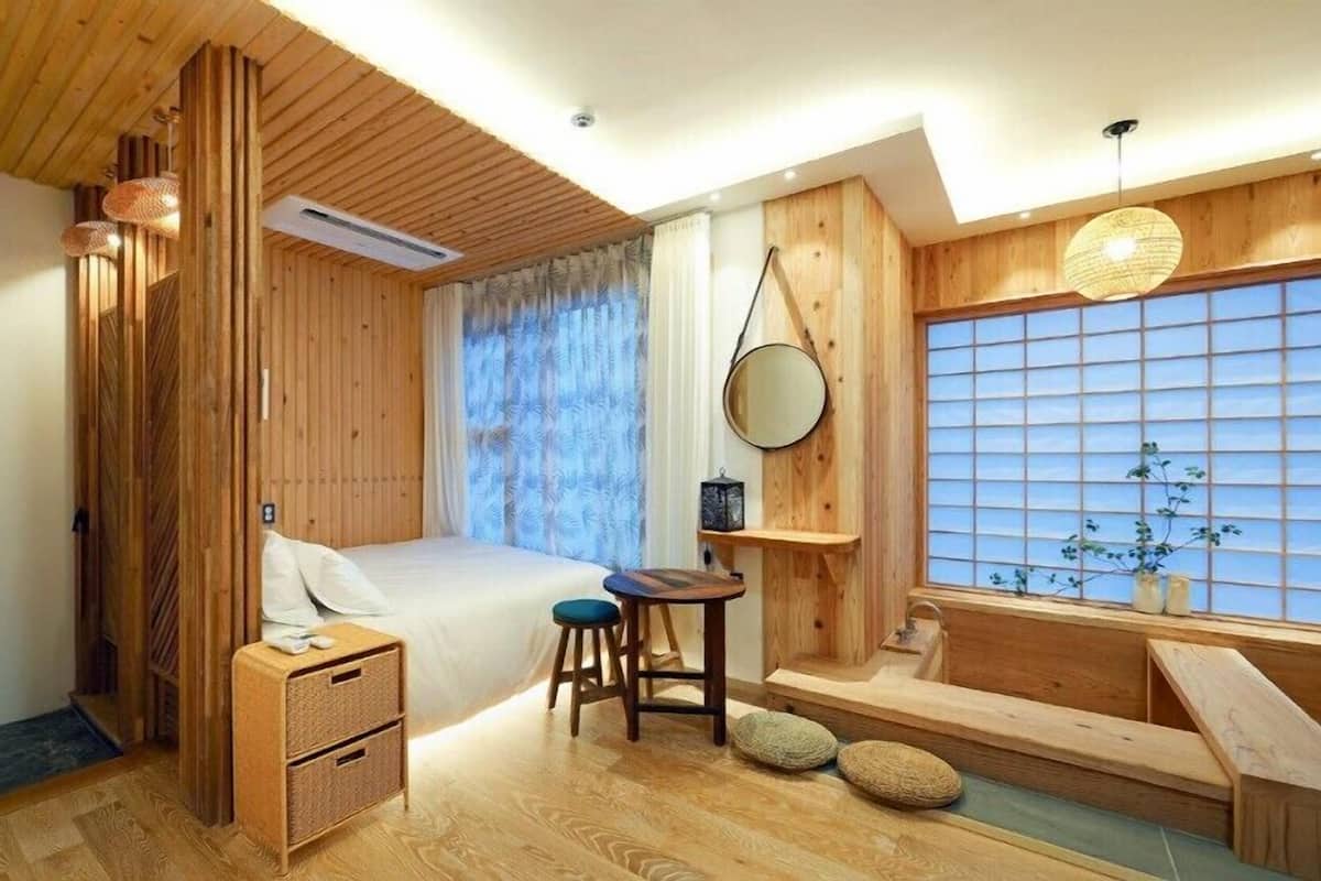 A wooden room with a bed, a small table, a chair, and a window with a view.