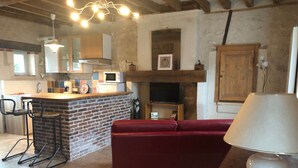 A kitchen with a brick island, bar stools, a red sofa, a TV, and a fireplace. - La Bergerie, Meublé de Tourisme*** for 4 people (Pontlevoy)