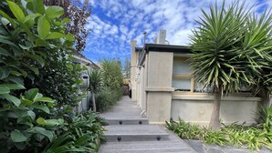 A wooden pathway leading to a modern house with a stone facade and a clear blue sky. - The Beach House At Henley (Henley Beach)