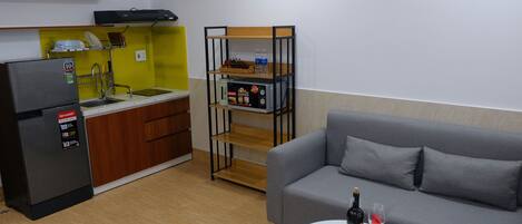 A compact living space with a kitchenette, grey sofa, and a small round table with a bottle and glass.