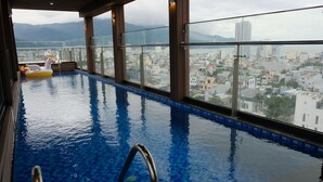 Una piscina interior con paredes de vidrio transparente, vistas a un paisaje urbano y un flotador hinchable con forma de unicornio.