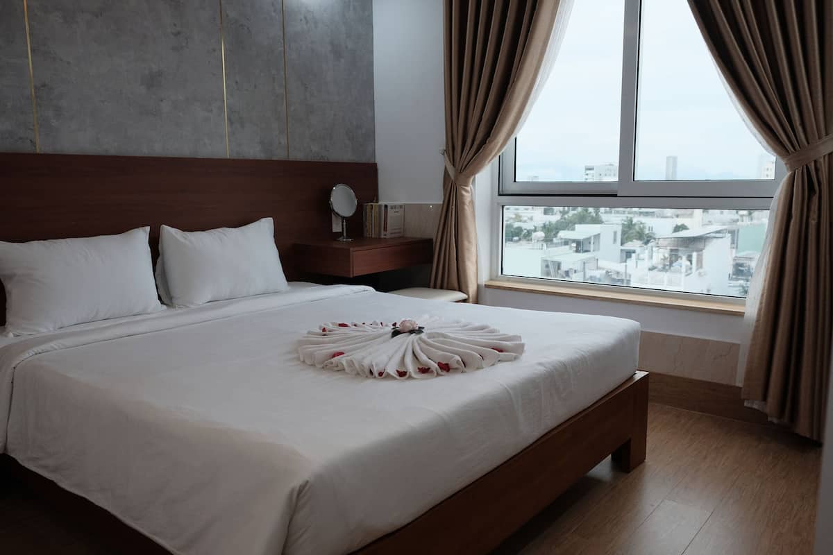 A neatly made bed with a decorative towel, a bedside table with a mirror and books, and a window with curtains.