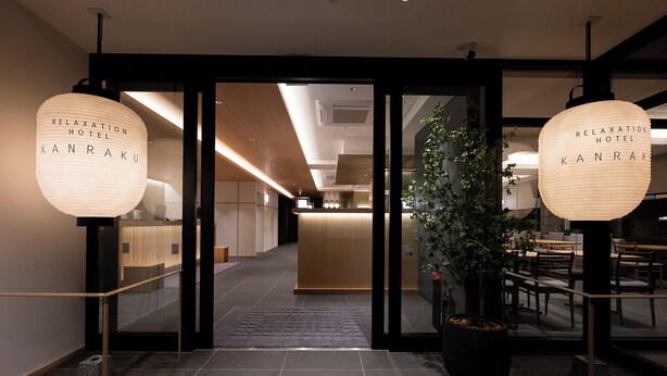 Eine Hotelrezeption mit modernem Design, inklusive einer Rezeptionstheke, einem Blumentopf und zwei großen Pendelleuchten mit dem Namen des Hotels.