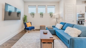 Un salon moderne avec un canapé bleu, un fauteuil bleu, une table basse et un téléviseur à écran plat fixé au mur.