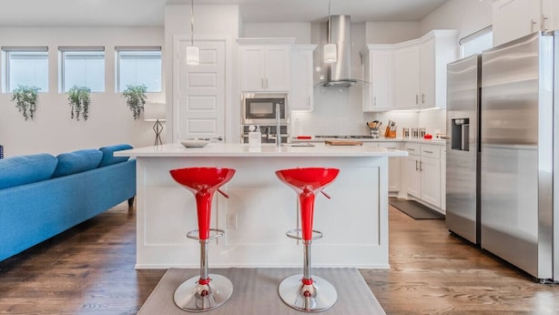 Une cuisine moderne avec des meubles blancs, un réfrigérateur en acier inoxydable et un îlot central doté de tabourets de bar rouges.