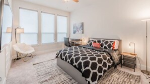 Une chambre moderne avec un grand lit, un bureau, une chaise et un ventilateur de plafond.