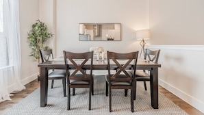 Un coin repas avec une table en bois foncé, quatre chaises, un grand miroir et une plante en pot.