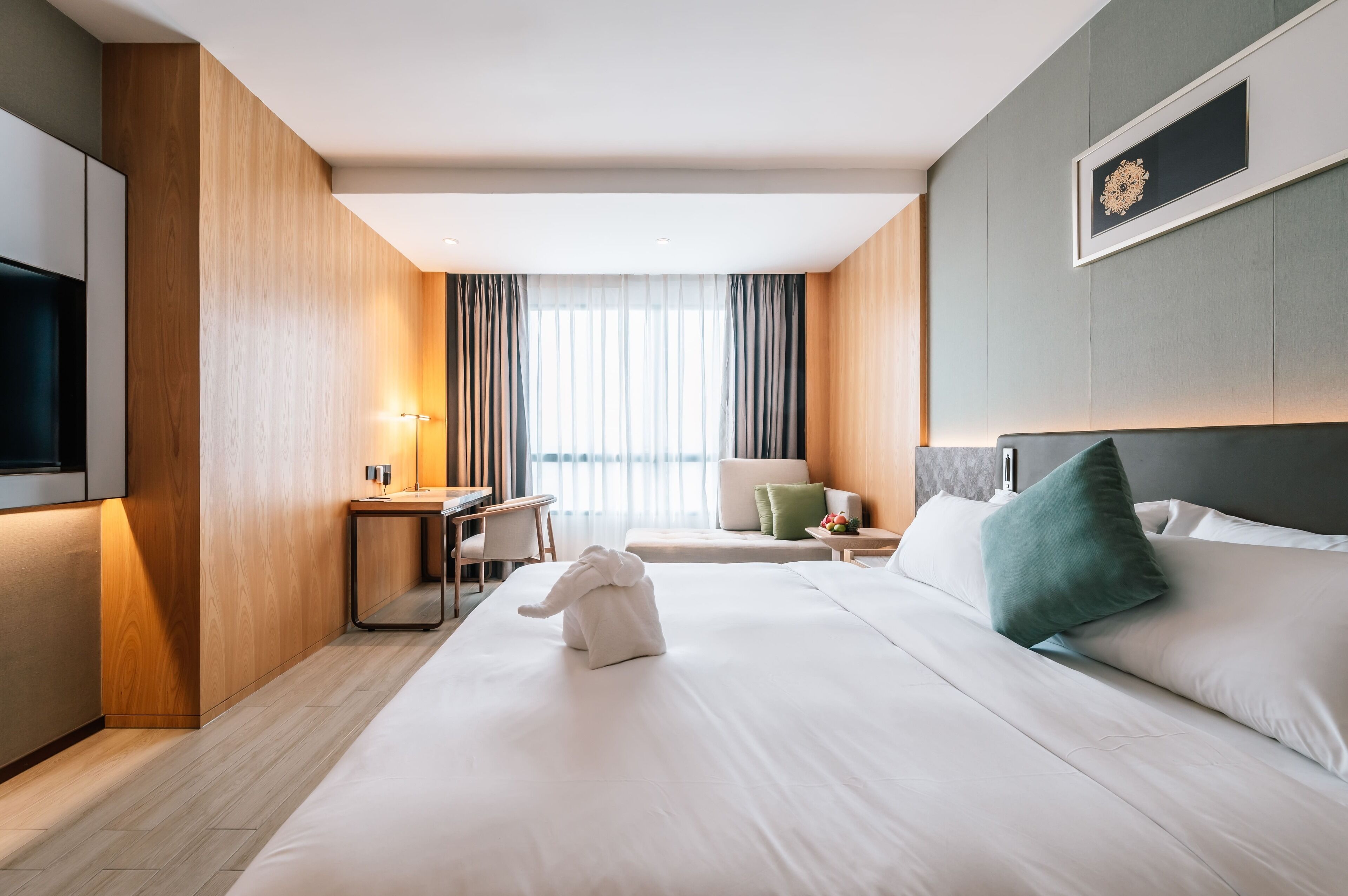 A hotel room with a bed, a desk, a chair, a TV, and a window with curtains.
