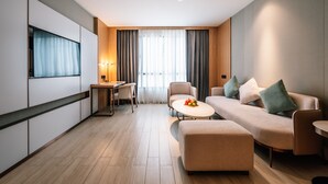 A modern hotel room with a sofa, ottoman, dining table, and a TV mounted on the wall. - Laike Hotel (Bangkok)