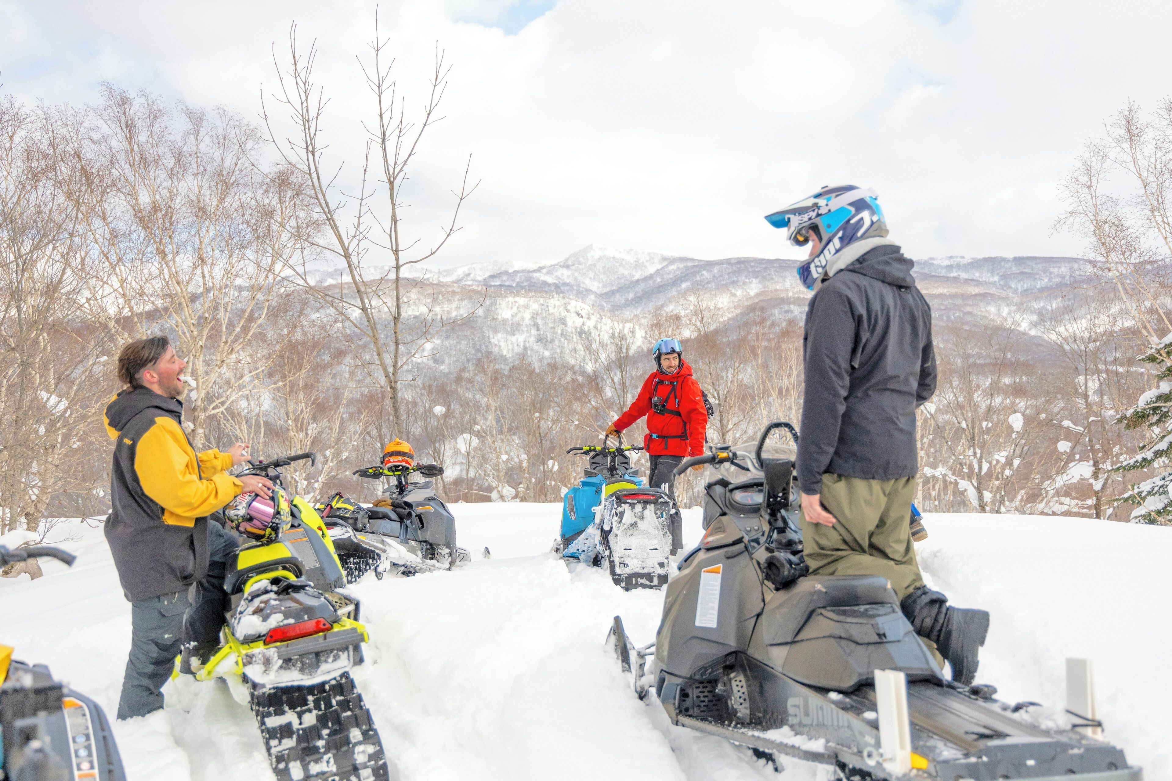 A group of people on snowmobiles in a snowy landscape with mountains in the background.