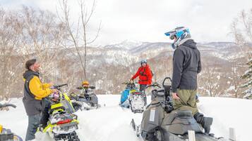 A group of people on snowmobiles in a snowy landscape with mountains in the background.