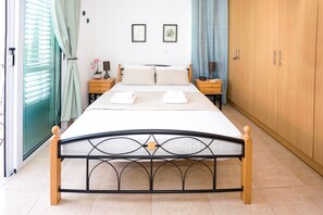 A neatly made bed with pillows and towels, wooden nightstands with lamps, a wardrobe, and a window with curtains.