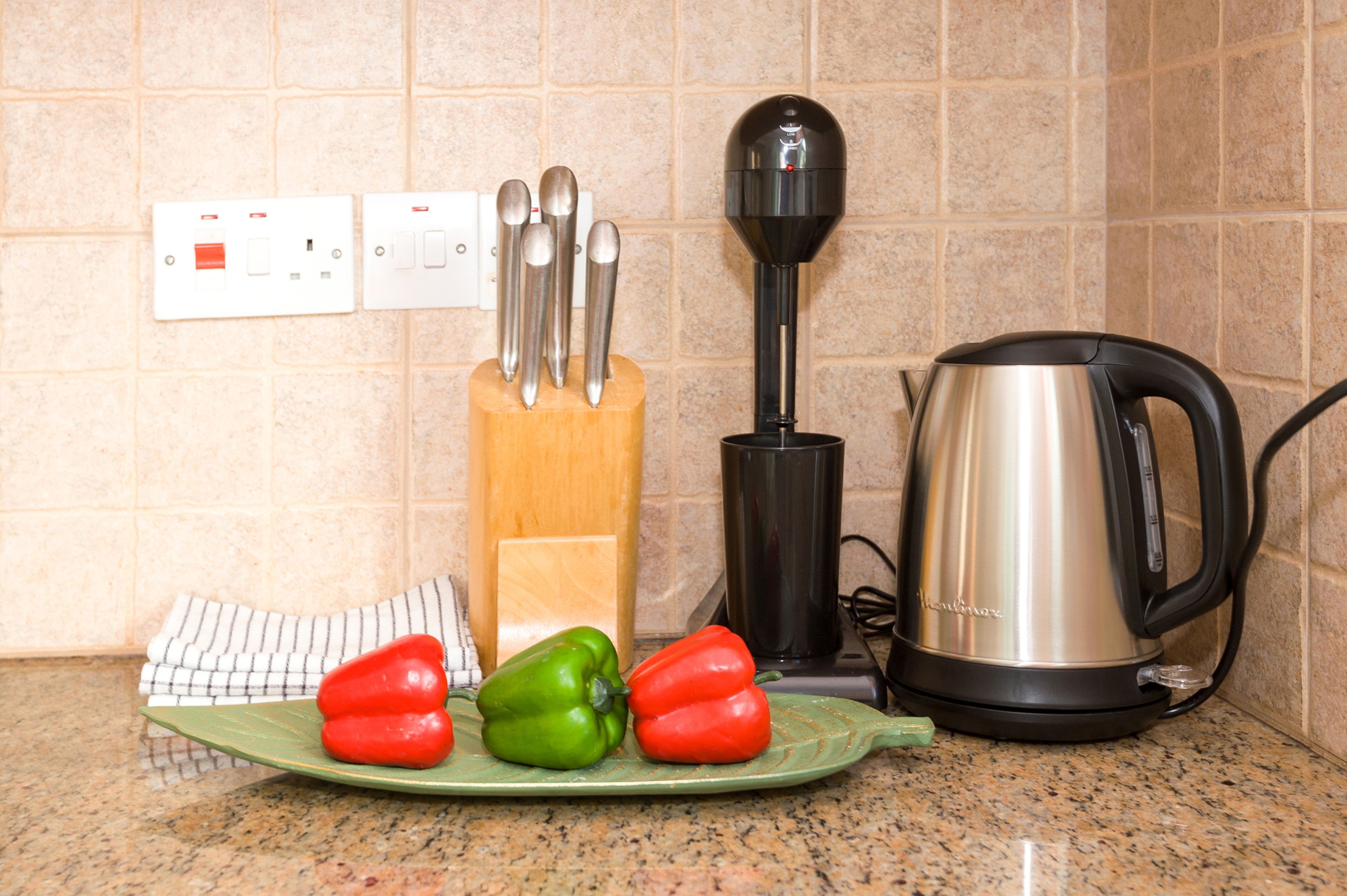 Een keukentafel met een bord vol paprika's, een koffiezetapparaat en een messenblok.