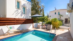 Una piscina con borde de azulejos, cubierta de madera y mobiliario exterior.