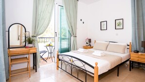 Un dormitorio con cama, mesitas de noche, escritorio, silla, espejo y balcón con mesa y sillas.