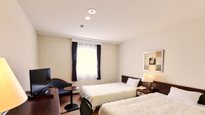 Ein Hotelzimmer mit zwei Betten, einem Schreibtisch mit Computer, einem Stuhl und einem kleinen Tisch.