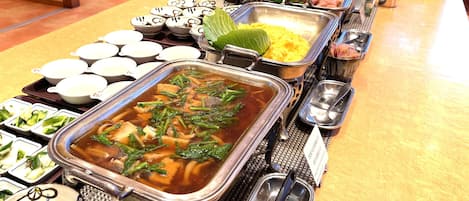 A buffet with various dishes including a large pot of soup, several trays of food, and multiple bowls.