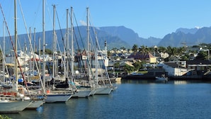 Un port de plaisance où sont amarrés de nombreux voiliers, avec une chaîne de montagnes en arrière-plan et des immeubles résidentiels à proximité.