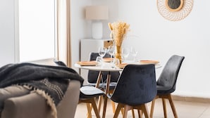 Un coin repas avec une table ronde dressée pour quatre personnes, entourée de chaises aux couleurs sombres.