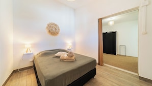 Une chambre à coucher avec un lit, des lampes de chevet, un élément décoratif fixé au mur et un grand miroir qui reflète une porte et un rideau.