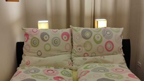 Un lit avec une couvre-lit à motifs et des oreillers, deux lampes de chevet et une fenêtre avec des rideaux.