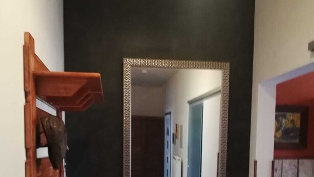 Un couloir avec un grand miroir, une étagère en bois, une extincteur rouge et un tapis à motifs.