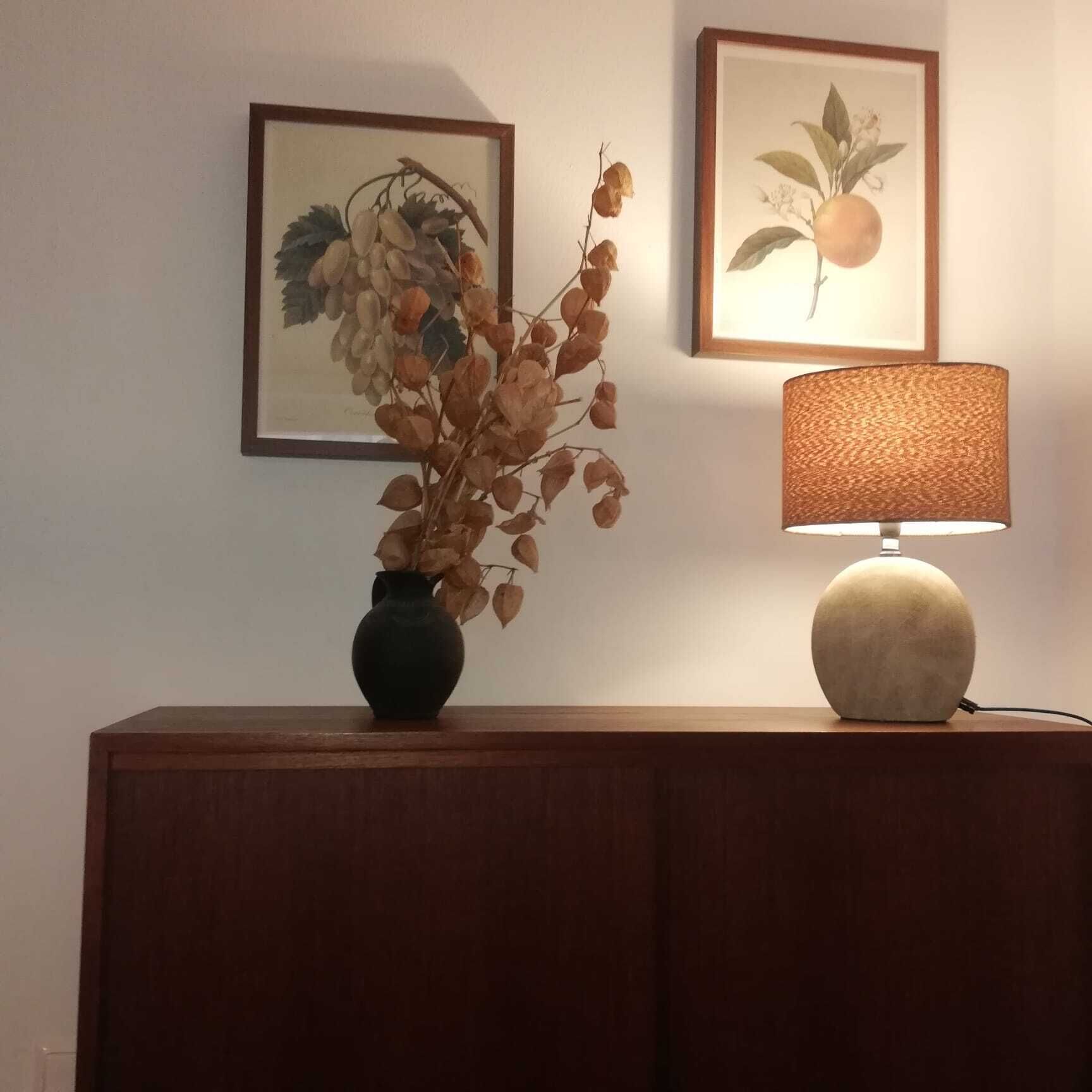 Ein Holzkabinet mit einer Vasen voller getrockneter Blumen und einer Lampe mit einer strukturierten Lampenschirm.