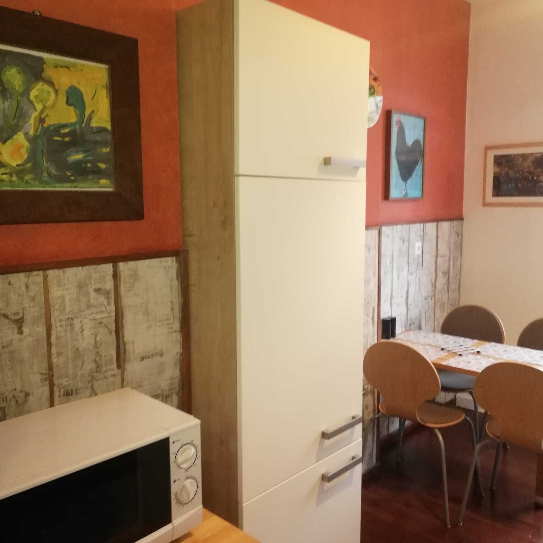 Una cocina con un refrigerador blanco, un microondas y una mesa de comedor con cuatro sillas.