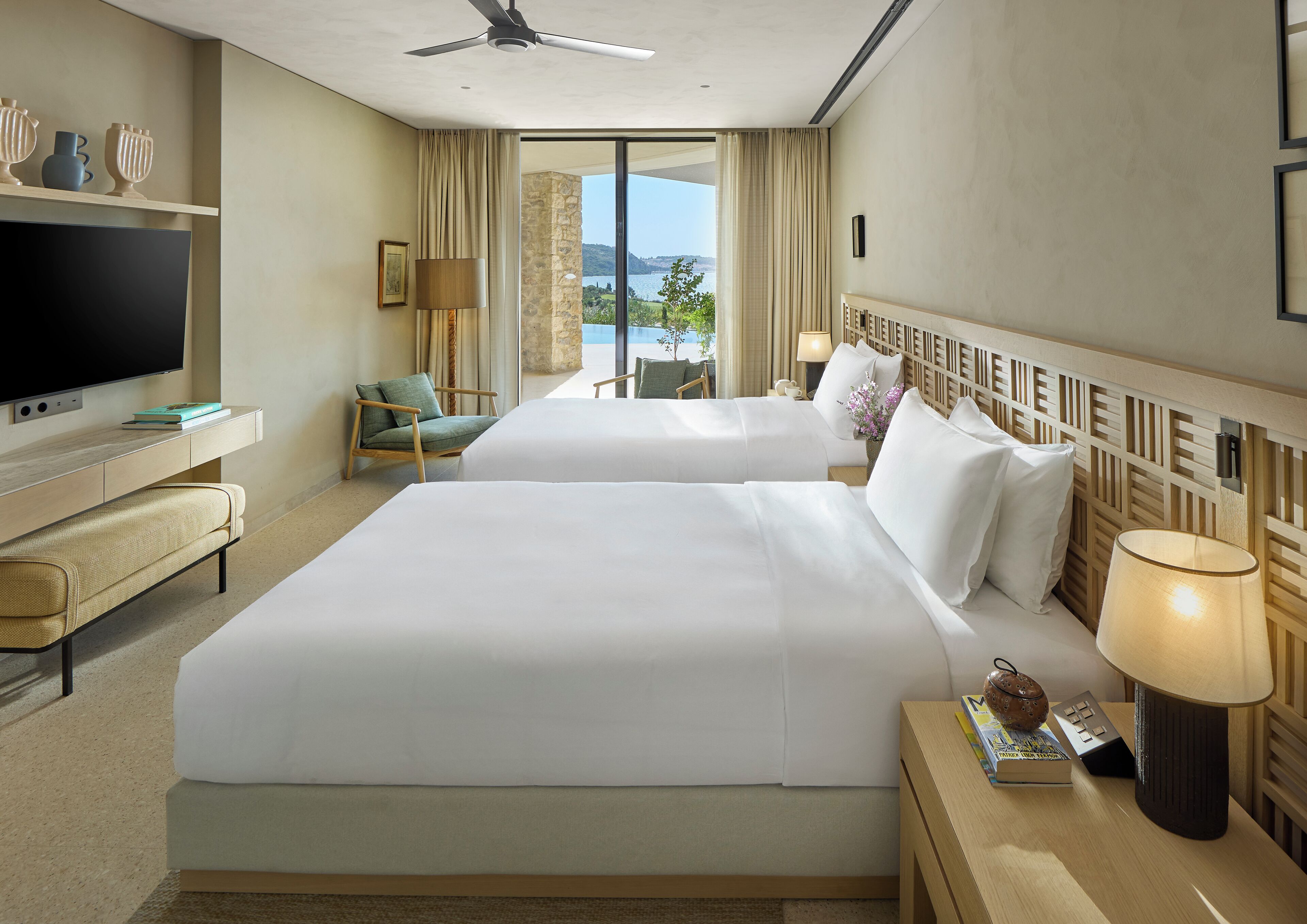 Habitación de hotel con dos camas, televisión, escritorio y vista al mar.